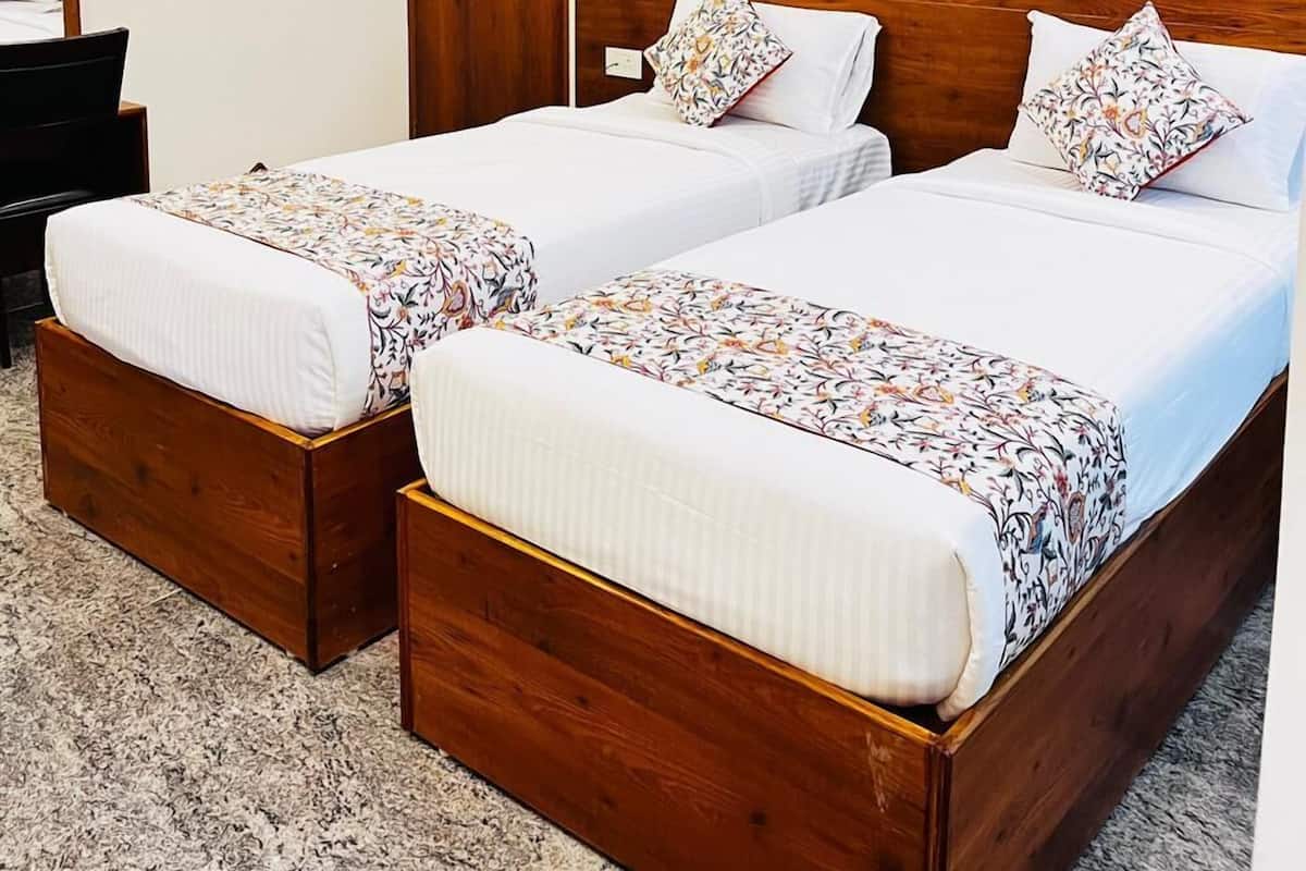 A hotel room with two wooden beds, a ceiling fan, a painting on the wall, and a desk with a chair.