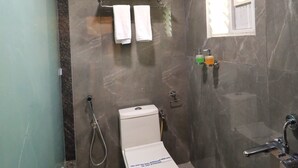 Un baño moderno con cabina de ducha de vidrio, un inodoro con una nota en la tapa y un perchero con dos toallas.