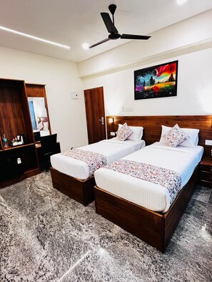 A hotel room with two single beds, a ceiling fan, a painting on the wall, and a wooden wardrobe. - Krishna's Inn (Sriperumbudur)