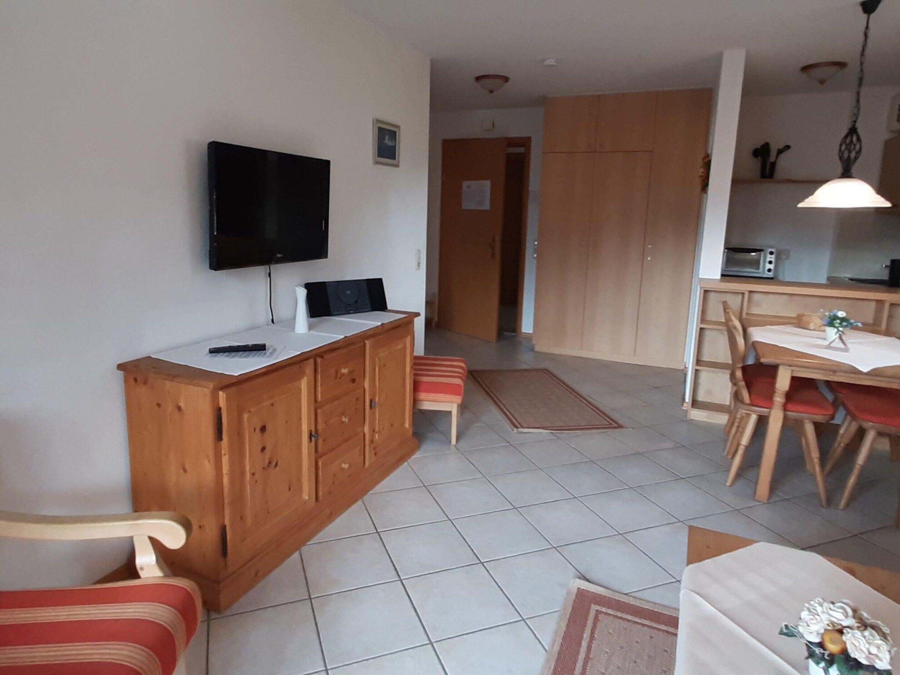 A compact living space with a kitchenette, a dining area, and a seating area with a TV mounted on the wall.