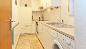 A compact kitchen with white cabinets, a built-in dishwasher, a washing machine, and a sink with a faucet.