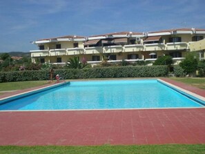Ein rechteckiger Swimmingpool mit roter Umrandung, umgeben von einer Rasenfläche und einer Reihe mehrstöckiger Gebäude mit Balkonen.