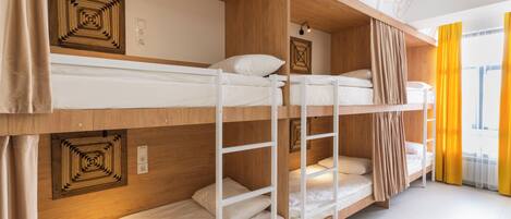 A bunk bed room with wooden walls and a ceiling with a geometric design. There are two beds, one on top of the other, and a window with yellow curtains.