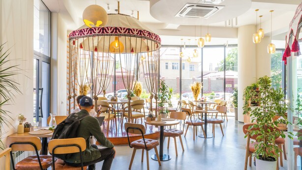 Un café moderne avec des tables et des chaises rondes, un luminaire suspendu et de grandes fenêtres.