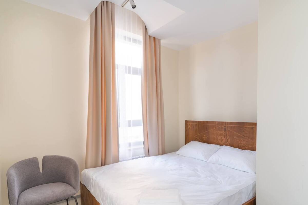 Una habitación de hotel con cama, una silla y una ventana con cortinas.