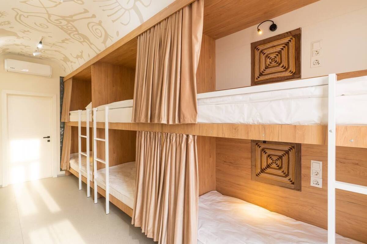 Habitación con literas, cabecera de madera, una escalera y una lámpara fijada a la pared.