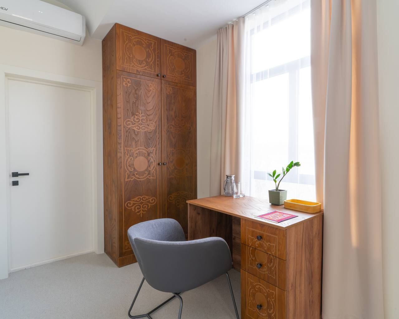 Una habitación con un armario de madera, un escritorio con silla, una ventana con cortinas y una planta pequeña en el alféizar.