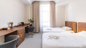 Une chambre d’hôtel avec un bureau en bois, deux lits, une chaise et une grande fenêtre avec des rideaux.