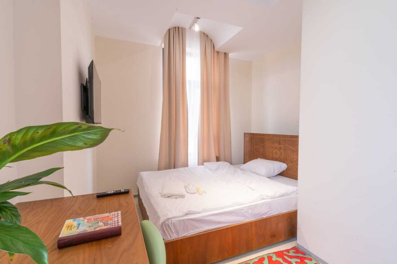 A hotel room with a bed, a TV mounted on the wall, a wooden table with a book, and a potted plant.