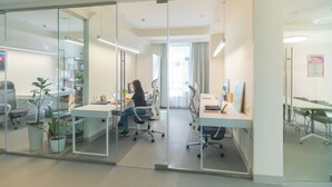 Un bureau avec des cloisons en verre, des bureaux blancs et des chaises de bureau.