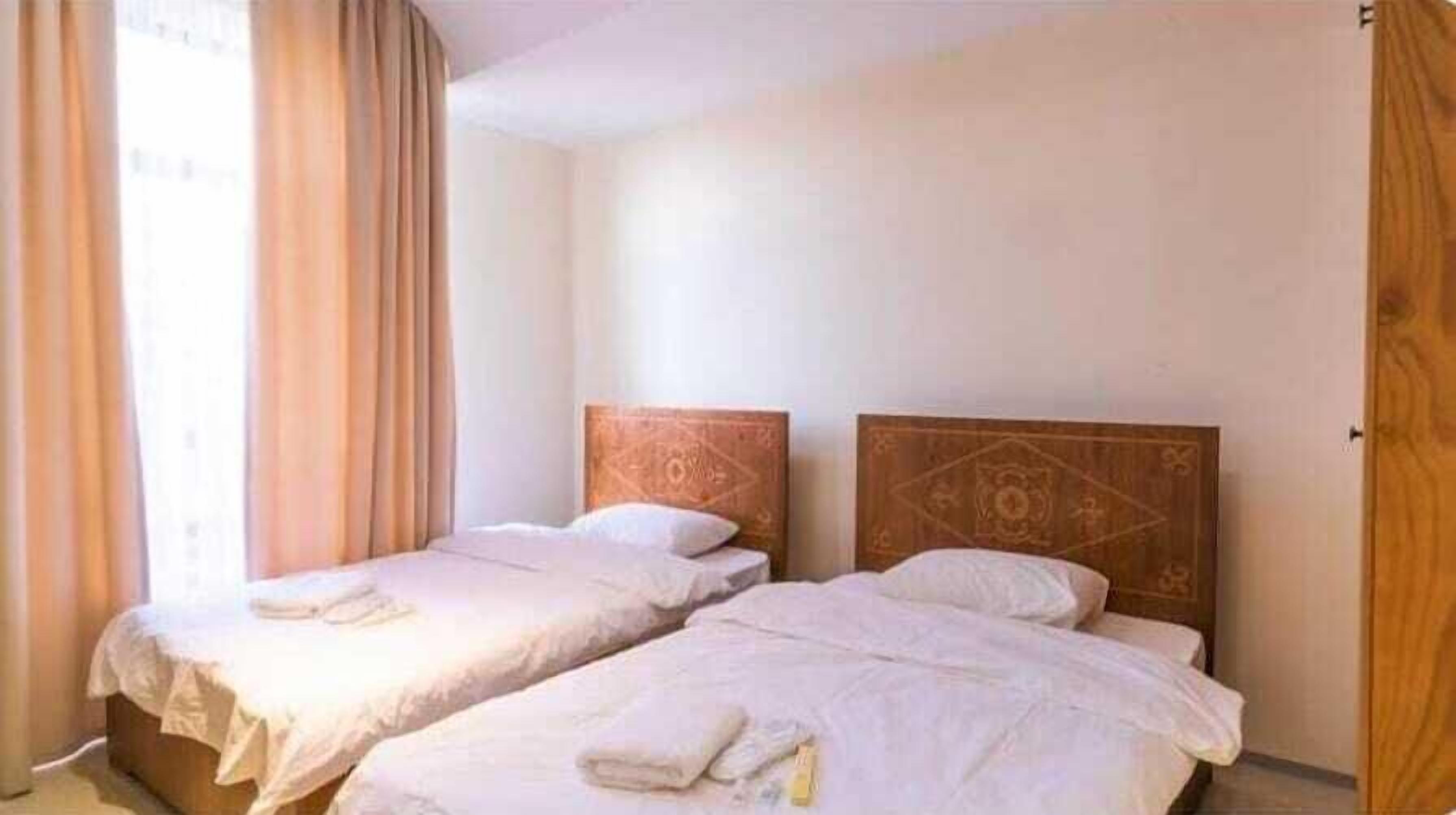 A room with two single beds, each with a wooden headboard and white linens.