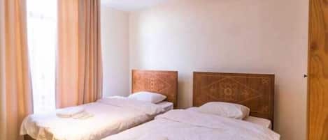 A room with two single beds, each with a wooden headboard and white linens.