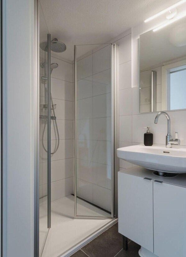 A modern bathroom with a glass-enclosed shower, a white sink, and a mirror above the sink. - Torbogenhuus No. 5 Comfortable Holiday Residence (Norderney)