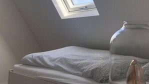 Ένα υπνοδωμάτιο με φεγγίτη, ένα κρεβάτι και ένα φωτιστικό.