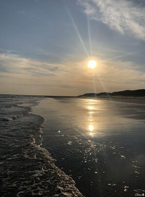 A beach with the sun setting over the horizon, creating a calm and reflective water surface. - Torbogenhuus No. 5 Comfortable Holiday Residence (Norderney)