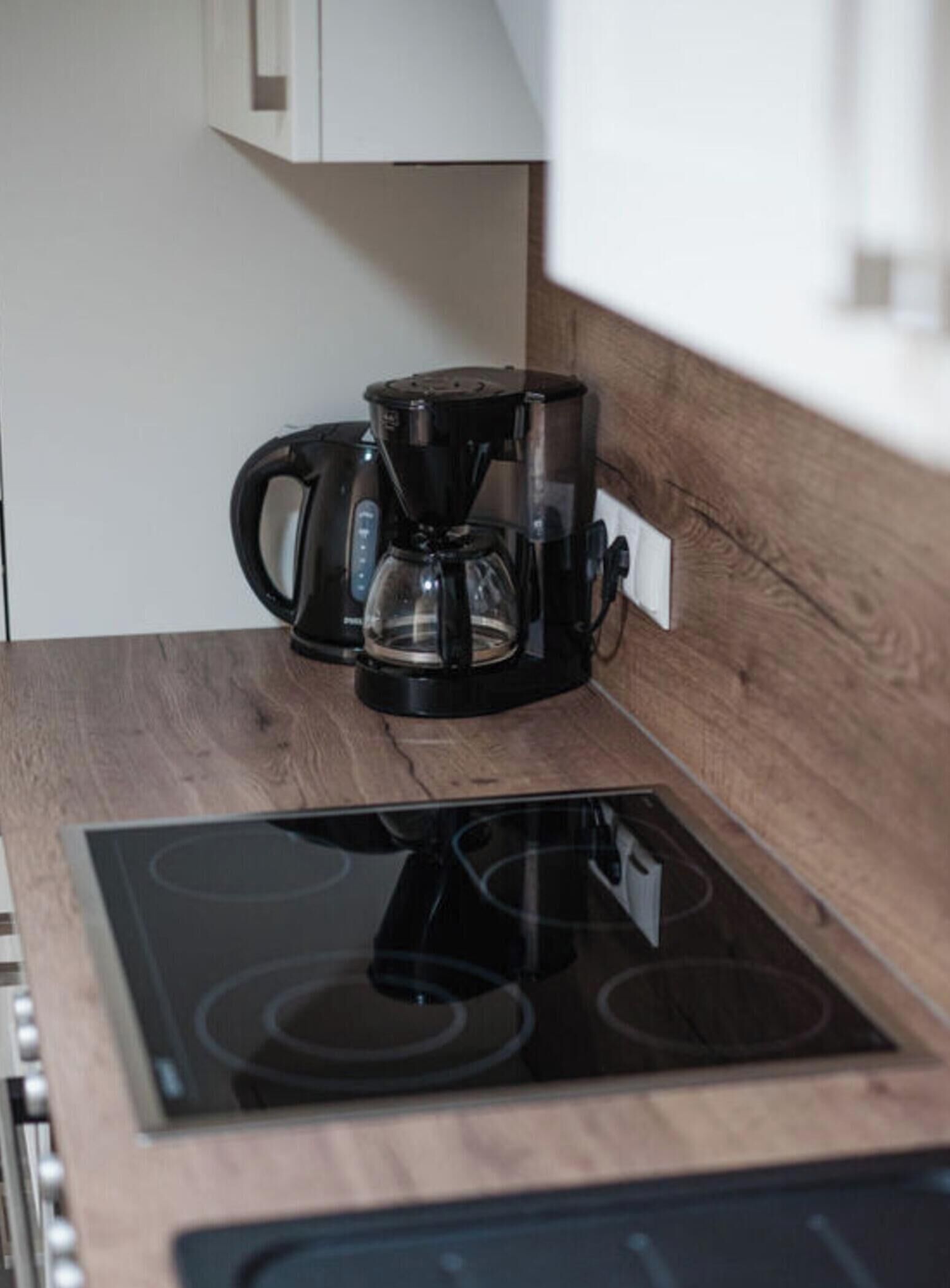 A kitchen with a black coffee maker on a wooden countertop and a black induction cooktop.