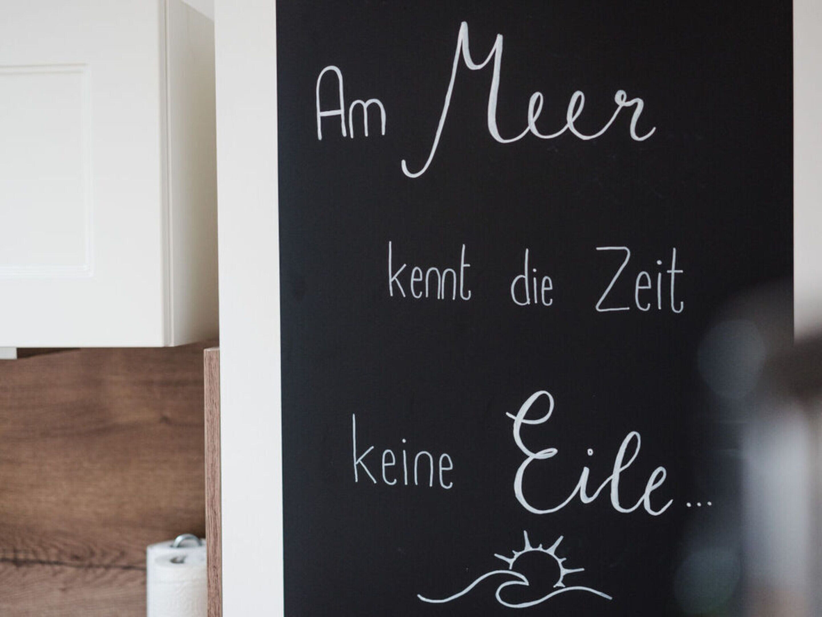 En tavle med teksten "Am Meer kennt die Zeit keine Eile..." skrevet i hvidt krudt.