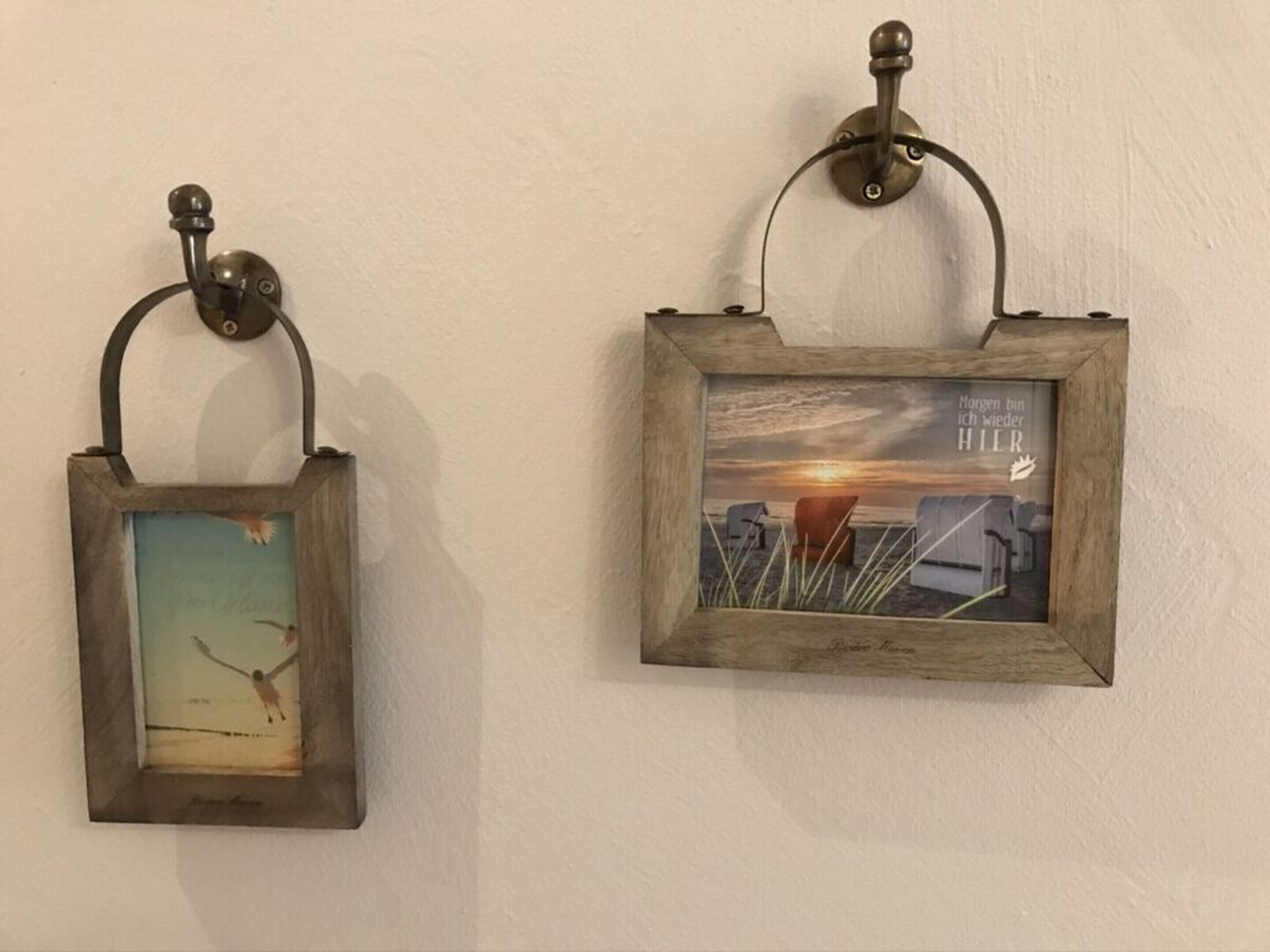 Two wall-mounted picture frames with rustic frames and metal hooks.