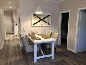 A dining area with a white table, beige chairs, and a pendant light. A framed sign with 'NAUTIC YACHT CLUB' hangs above the table.