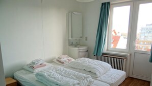 A hotel room with two beds, a window with curtains, a radiator, and a small bedside table. - Picturesque Apartment in Nieuwpoort (Nieuwpoort)