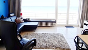 A modern living room with a sofa, a chair, a table, and a view of the sea through large windows. - Picturesque Apartment in Nieuwpoort (Nieuwpoort)