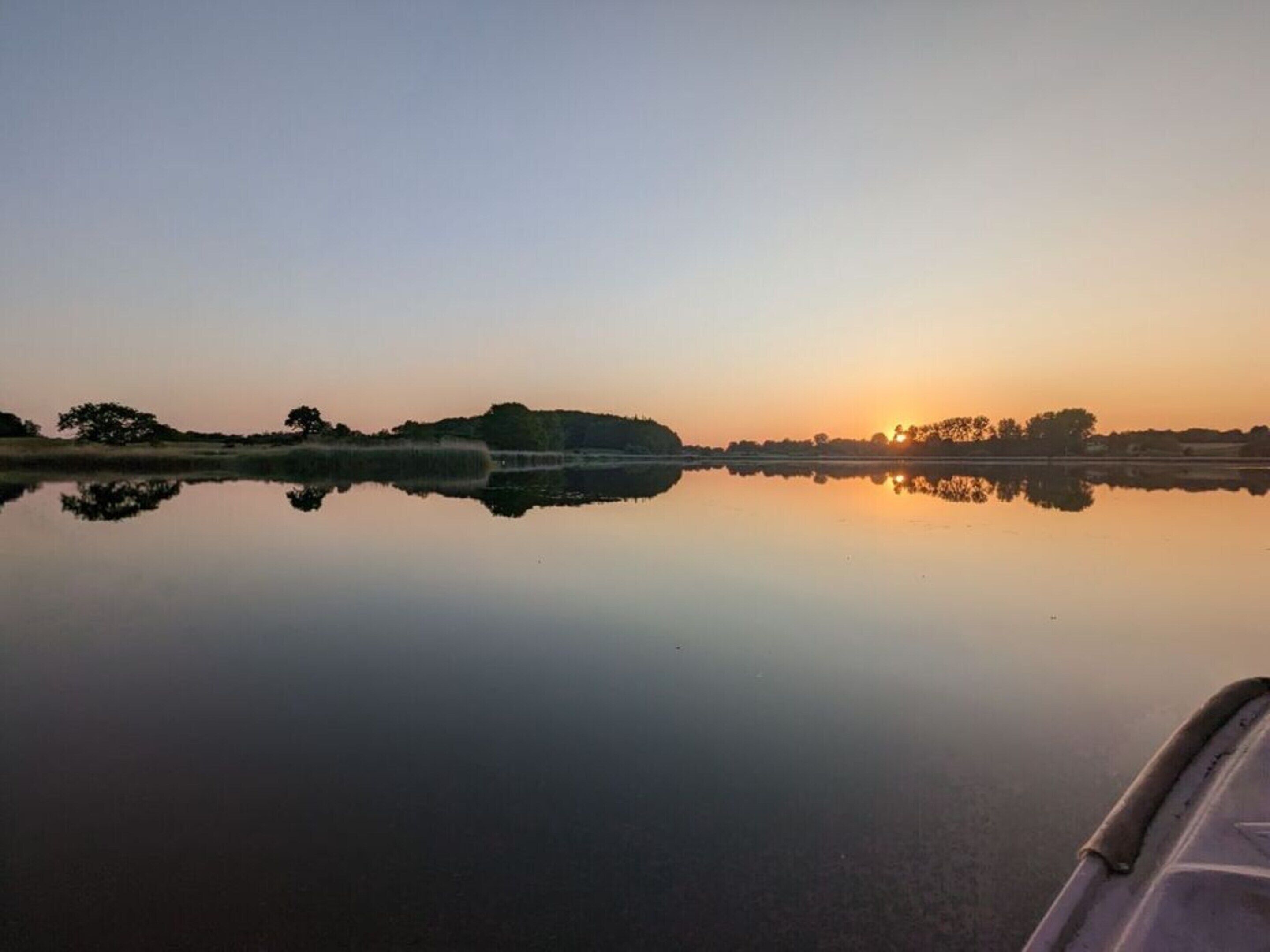 Een rustig meer bij zonsopgang, met een boot op de voorgrond.