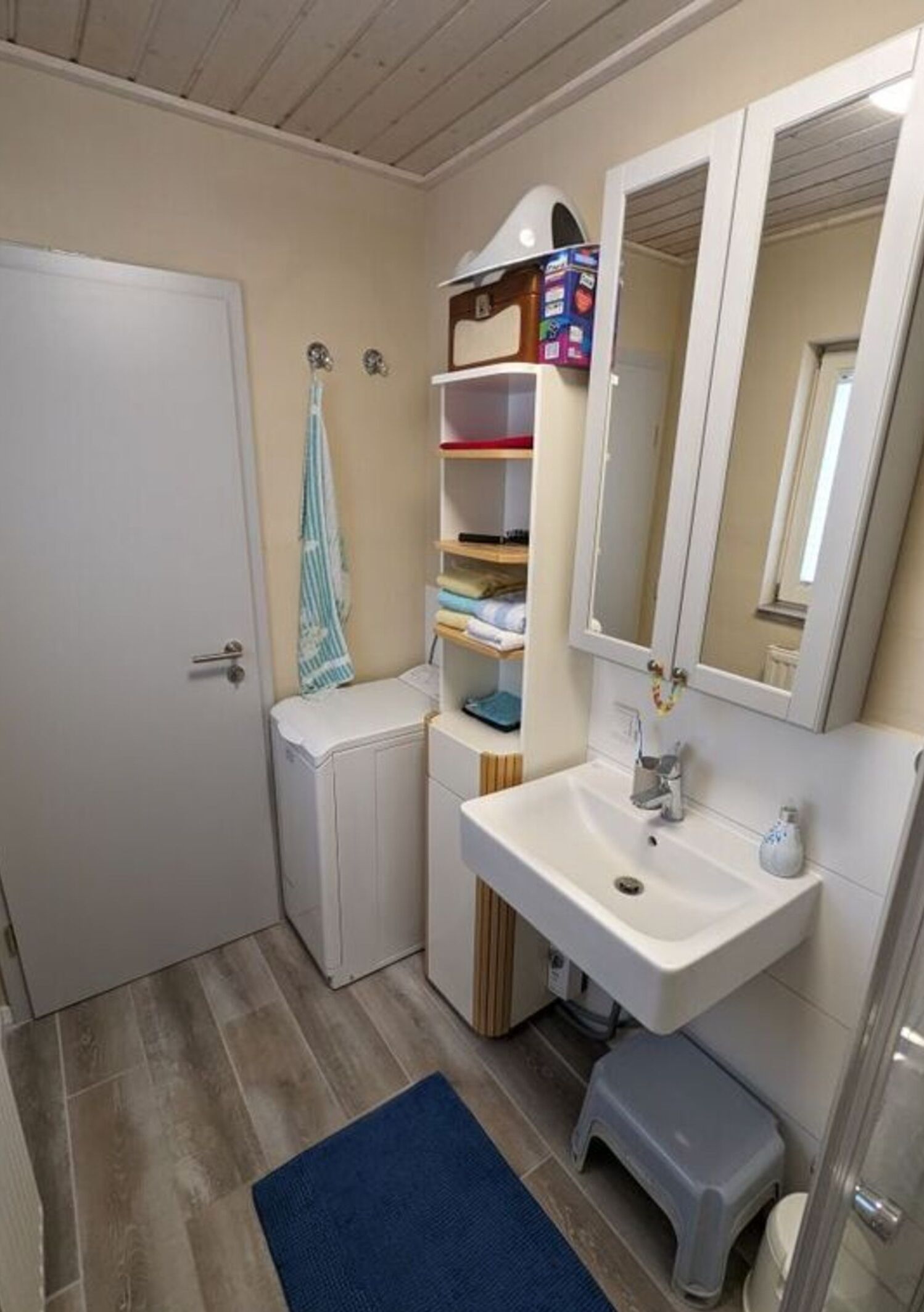 A compact bathroom with a white sink, a mirror, a towel rack, and a small storage unit.