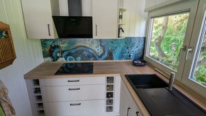 A compact kitchen with white cabinetry, a black stove, and a backsplash with a blue abstract design. - Schleipanorama Modern Retreat (Brodersby)