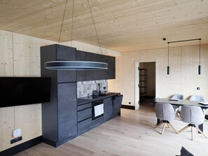 Et moderne køkken med indbygget ovn, stor sort emhætte og spiseplads med bord og stole.