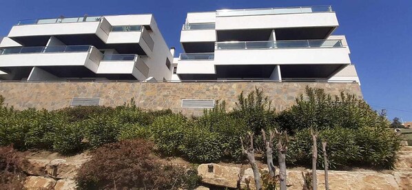 A modern multi-story building with balconies and a stone facade. - Sunny Garden Apartment (Casares)
