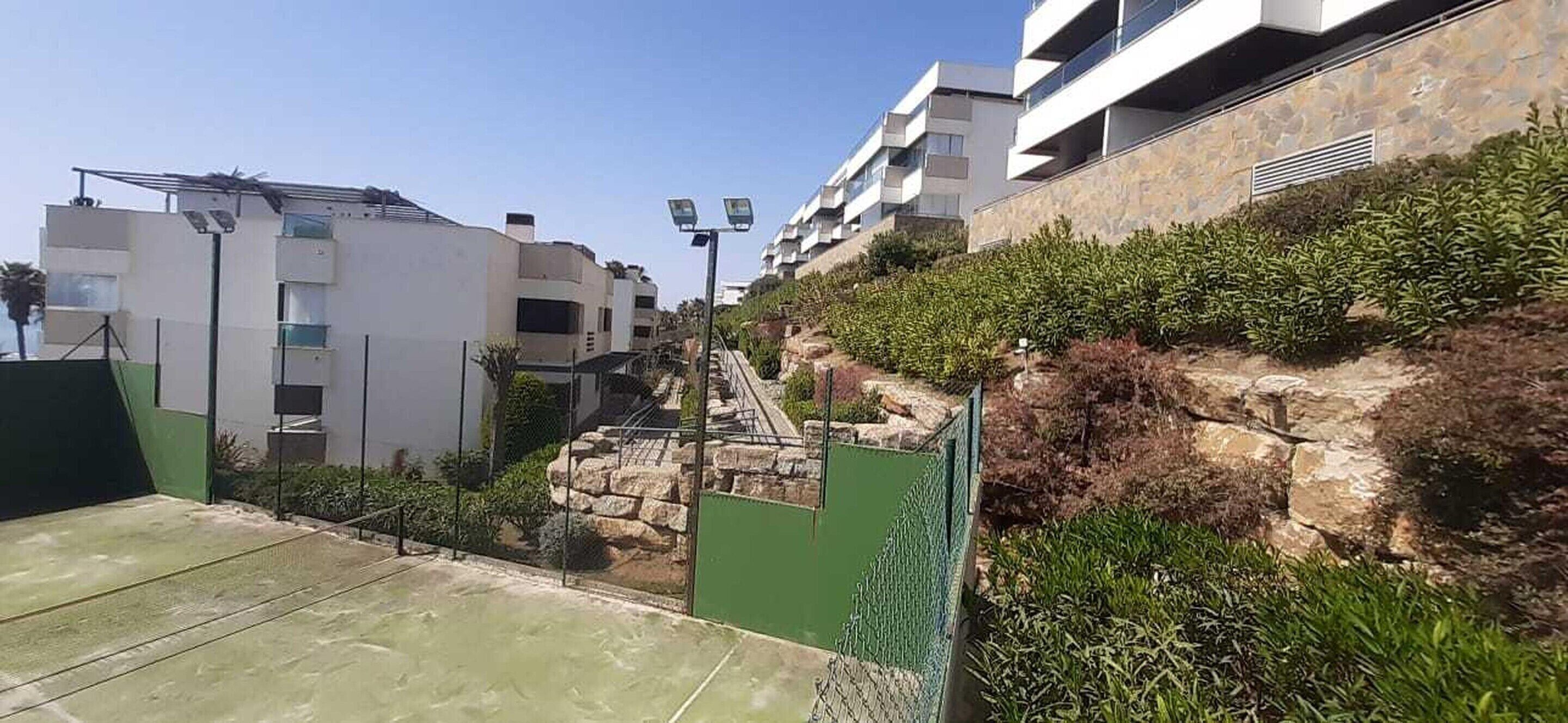 Zona residencial con edificios modernos, un muro de piedra y un portón verde.