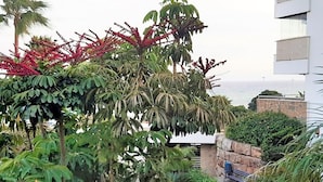 A balcony with lush tropical plants and a view of the sea. - Sunny Garden Apartment (Casares)
