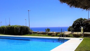 A swimming pool with a clear view of the ocean in the background. - Sunny Garden Apartment (Casares)