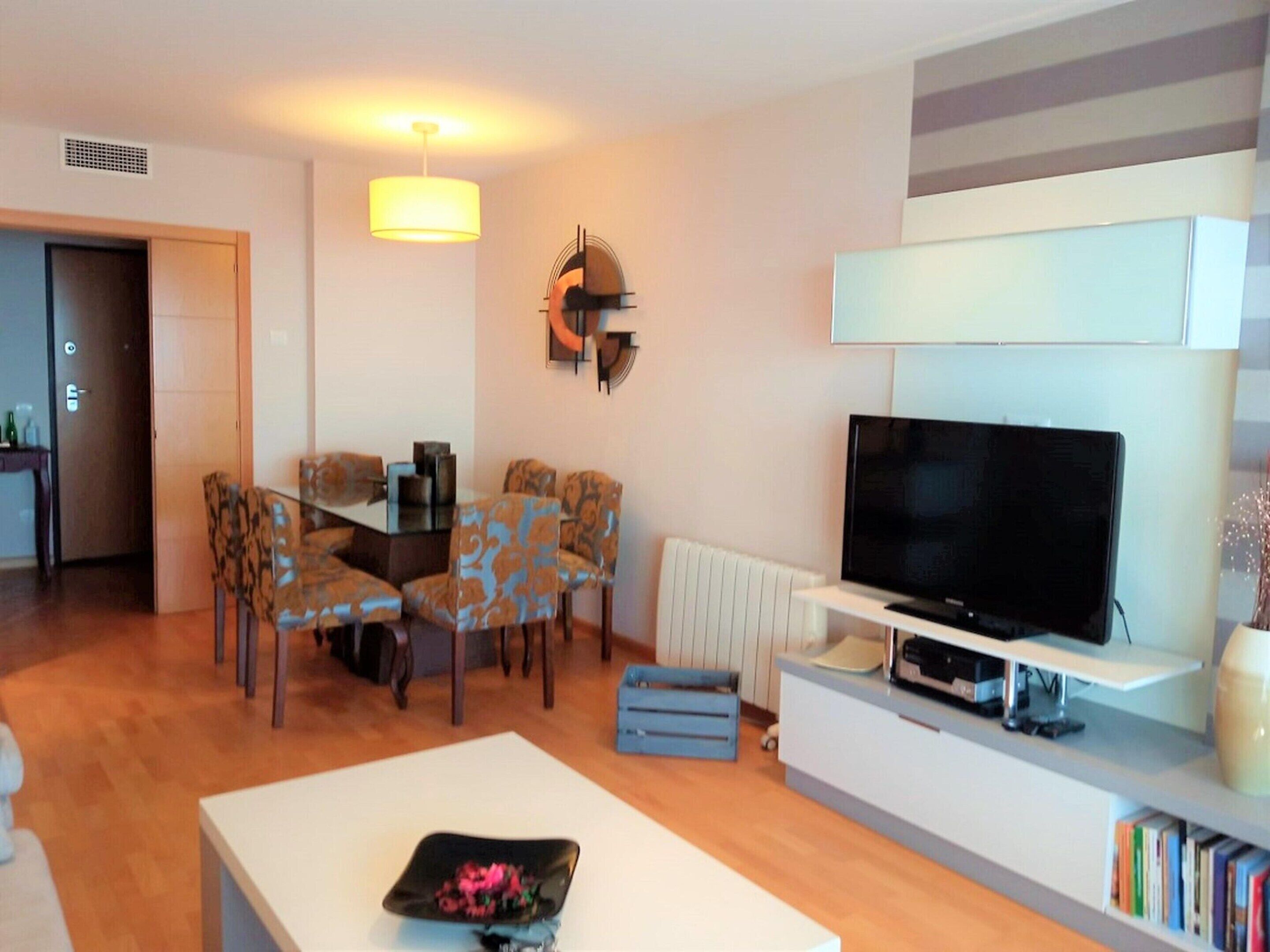 A modern living room with a dining area, a flat-screen TV, and a bookshelf.