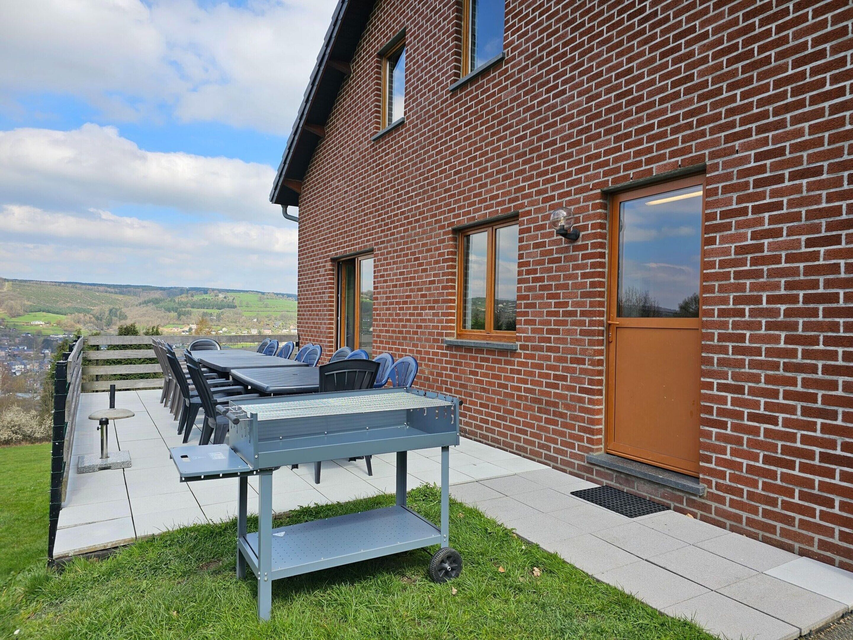 A brick building with a patio area featuring a table and chairs, a door, and windows.