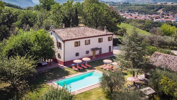 A two-story building with a swimming pool, surrounded by trees and a view of distant mountains. - Belvilla by OYO Villa Sapori (Pergola)