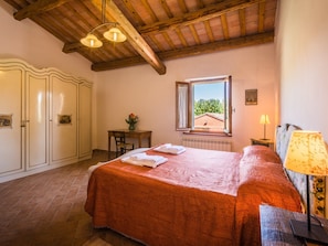 A bedroom with a bed, a wooden ceiling, a window with a view, a table with a vase, and a lamp. - Belvilla by OYO Villa Sapori (Pergola)