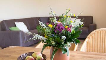 A dining table with a potted plant and a basket of apples.
