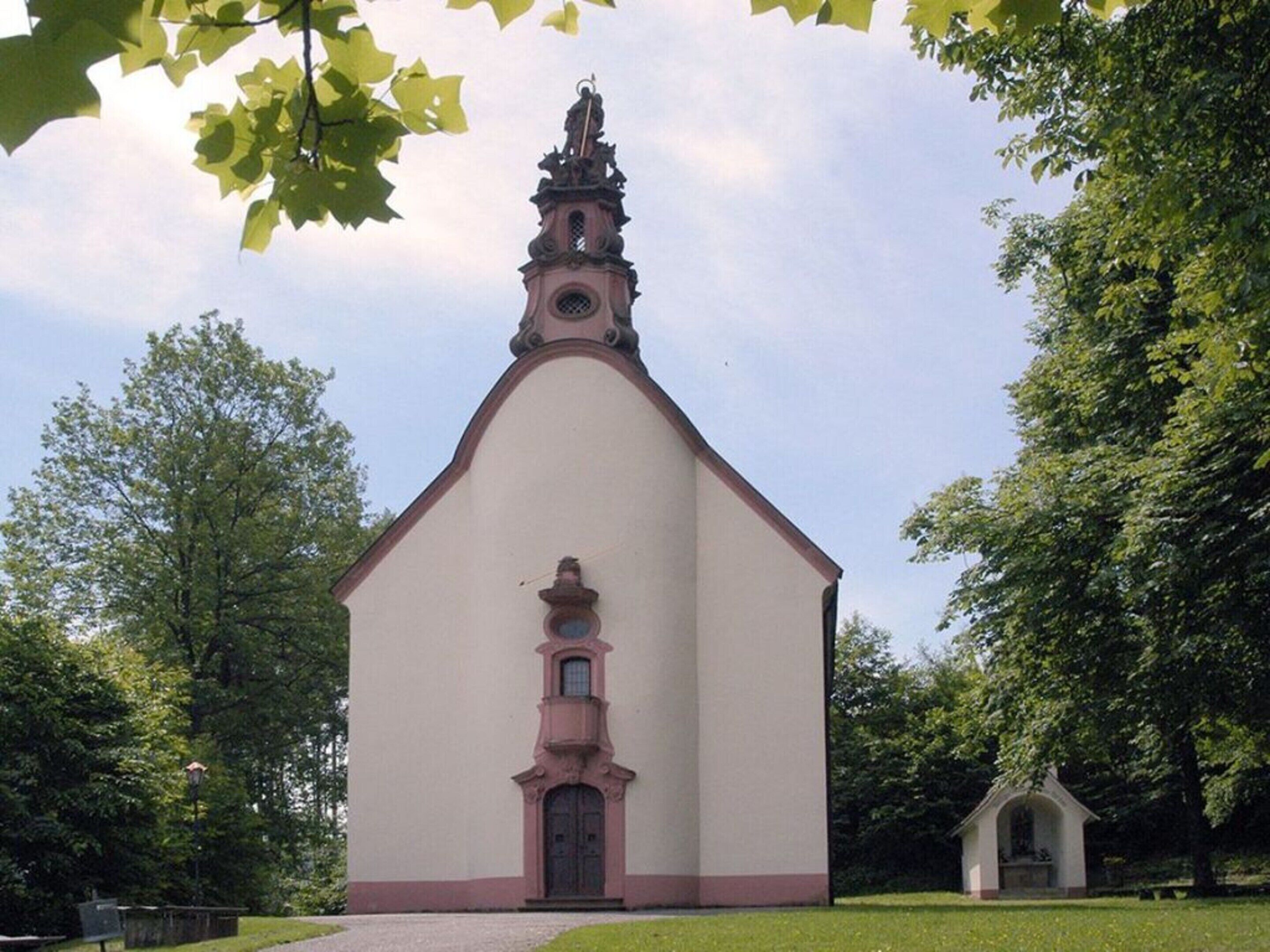 Eine Kirche mit einem hohen Kirchturm und einem kleinen Glockenturm, umgeben von Bäumen.