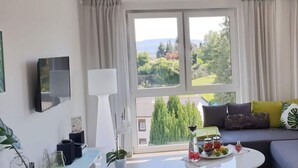 Una sala moderna con un ventanal grande, un sofá con cojines, una mesita de centro con una bandeja de frutas y una lámpara.