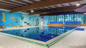Una piscina interior con un mural de vida marina en las paredes, vistas despejadas al exterior a través de amplios ventanales y un suelo de baldosas.