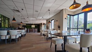 Un restaurante espacioso con techos altos, lámparas colgantes modernas y ventanas amplias que ofrecen vistas al exterior.