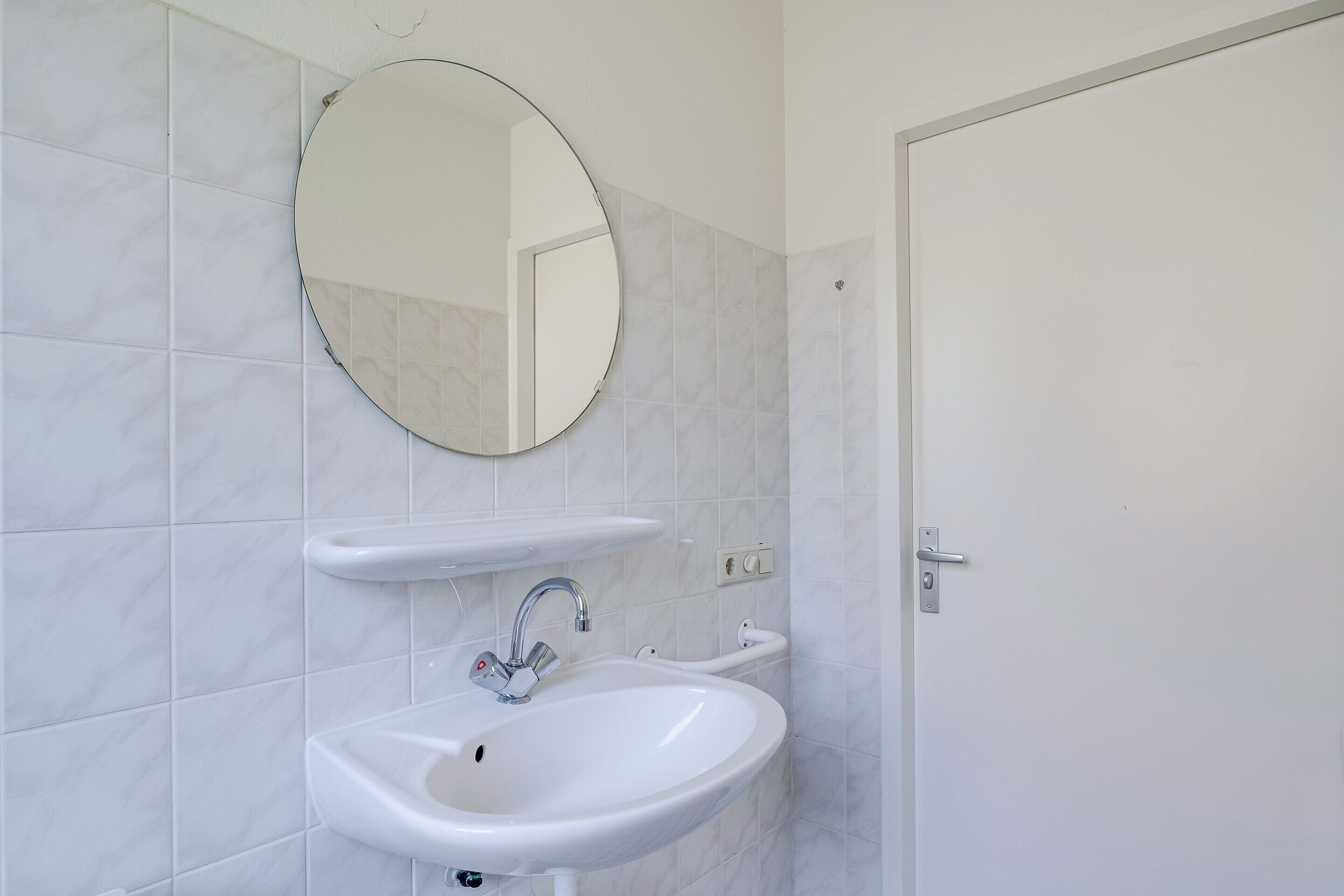 Een badkamer met een witte wastafel, een ronde spiegel en een deur.