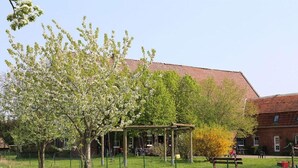 En park med gyngestativ, picnicbord og en bygning med rødt tag i baggrunden.