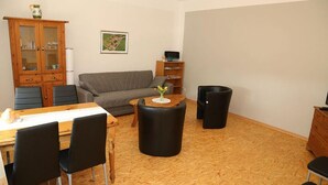 Un salon meublé comprenant un canapé, une table à manger avec des chaises, une table basse, un meuble et une poubelle.
