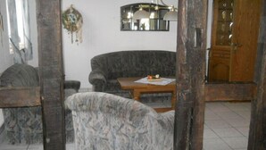 A room with a sofa, a small table with a placemat, a dreamcatcher on the wall, and a wooden cabinet. - Ferienhof Schwienhorst - Ferienwohnung Bauernstübchen. 1-7 Pers (Warendorf-Hoetmar)