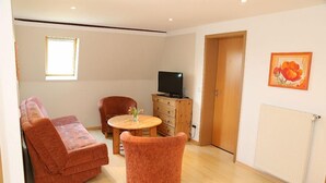 Un salon avec un canapé, une table ronde, un téléviseur posé sur un meuble en bois et une porte.