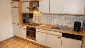 Une cuisine compacte avec des meubles blancs, un plan de travail en bois, un four à micro-ondes encastré, une cuisinière et un lave-vaisselle.