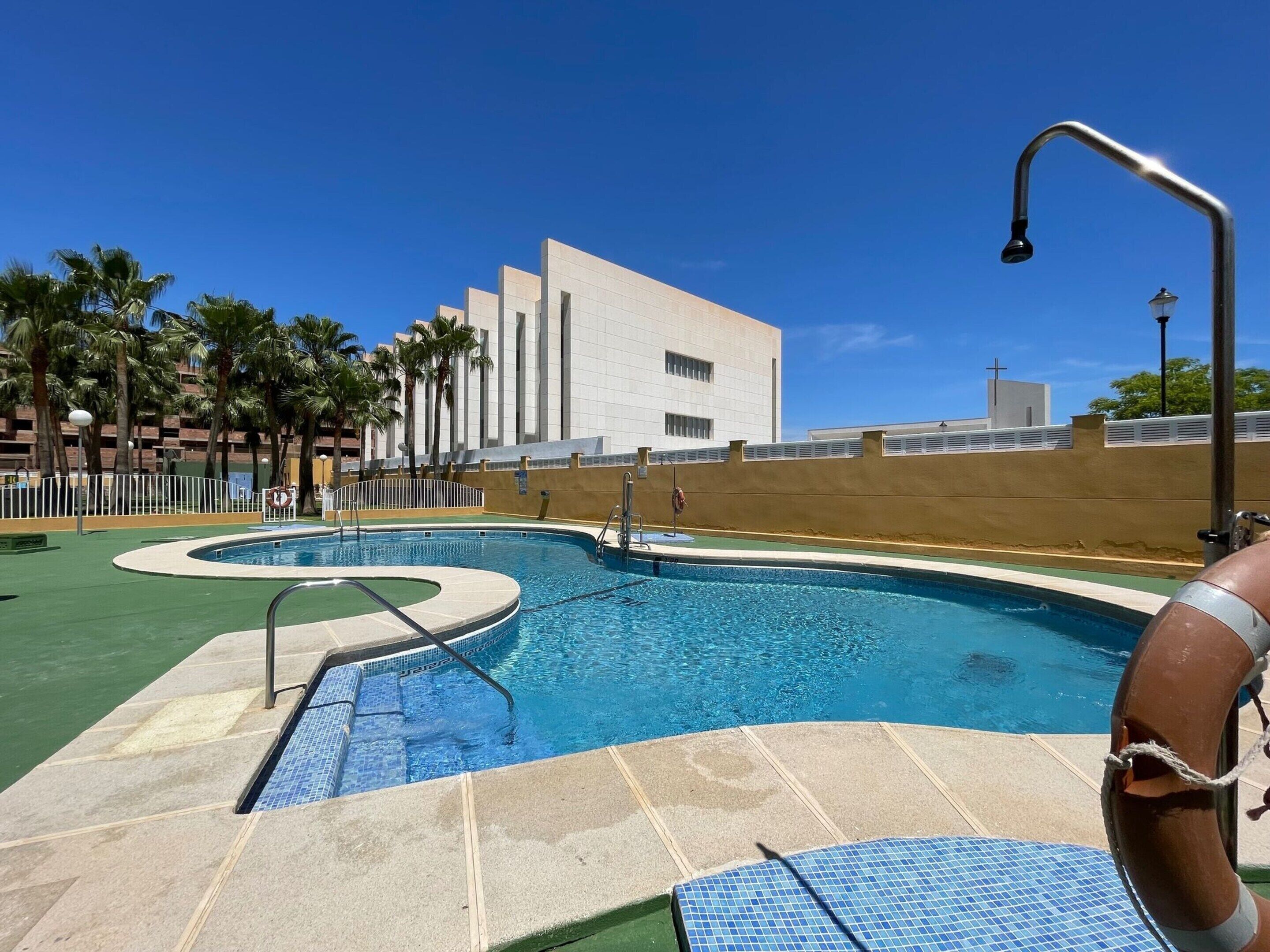 Una piscina con borde curvo, rodeada por un muro bajo y palmeras.