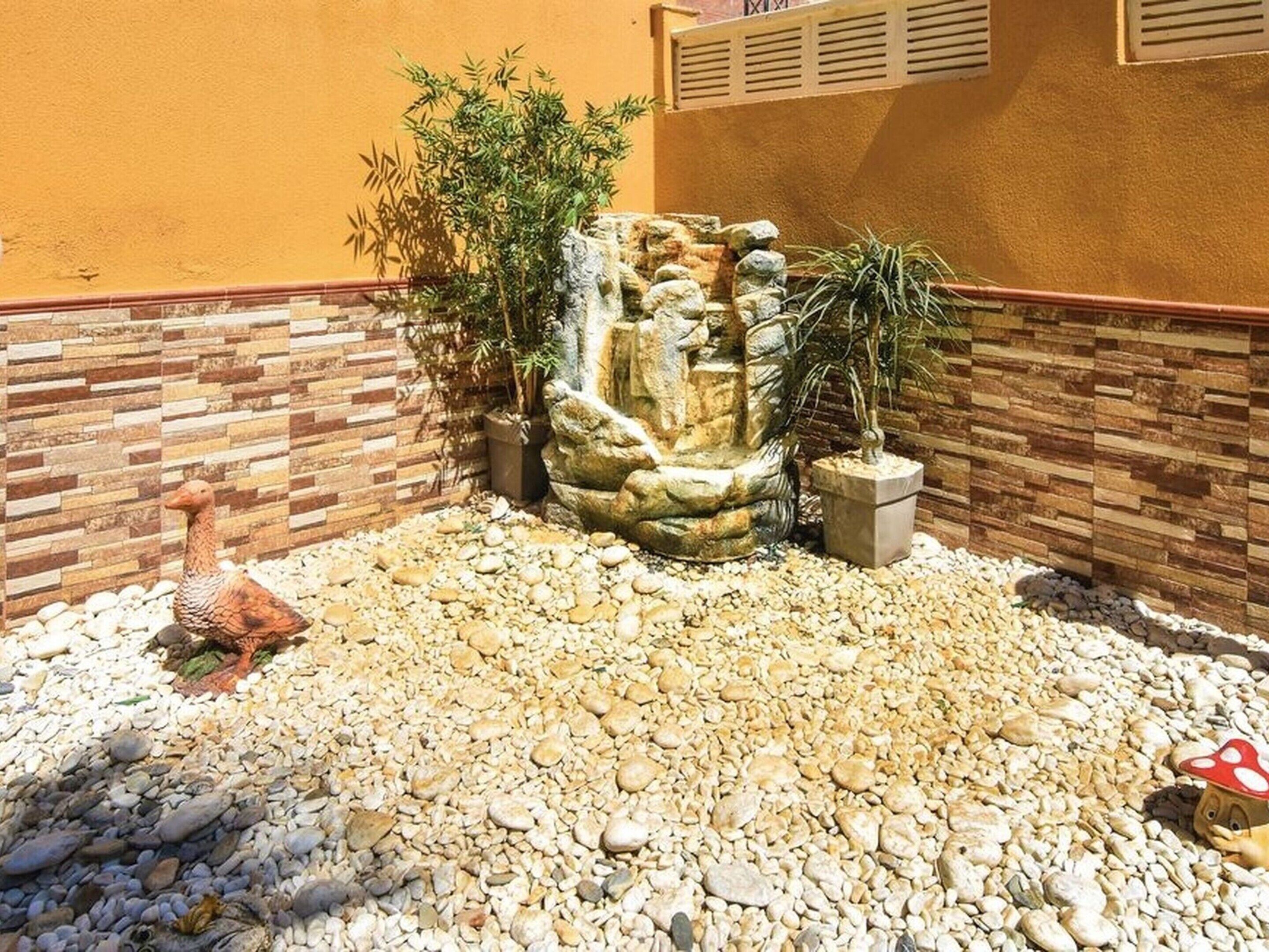Un jardín con una cascada de rocas, guijarros, una estatua de un ganso y un hongo.
